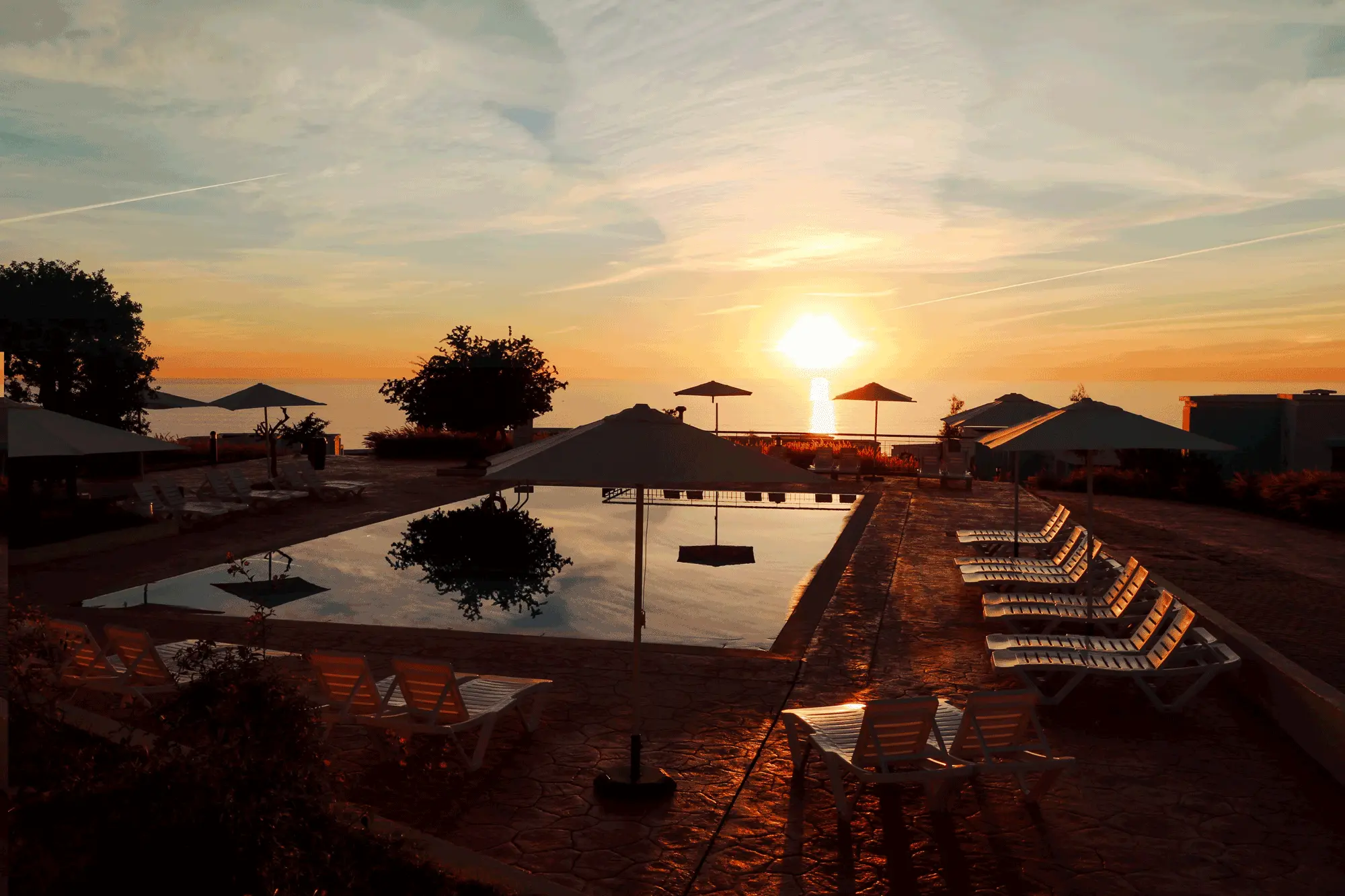 Piscine au coucher du soleil avec chaises longues et parasols